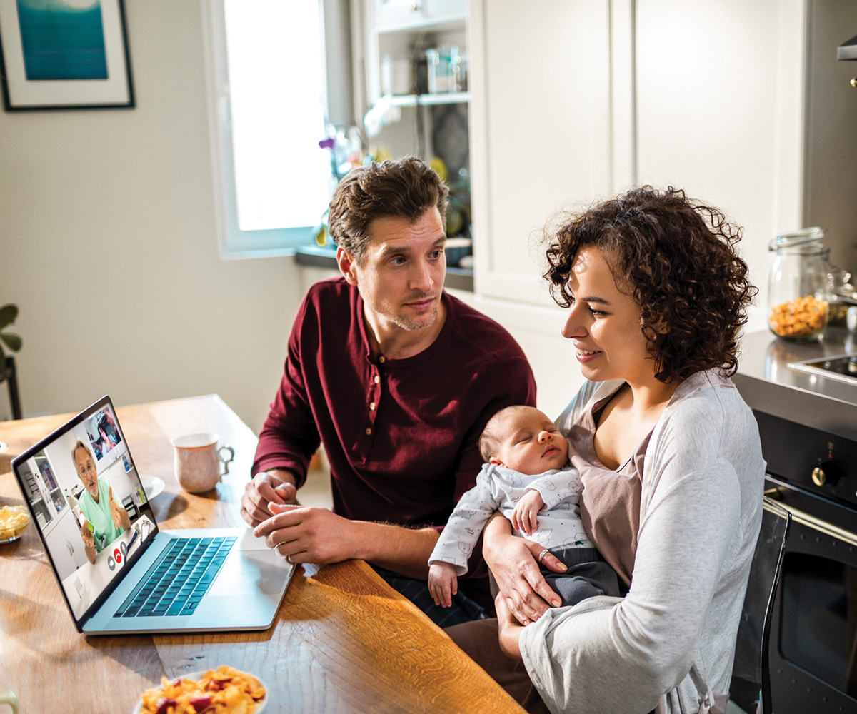 young father and mother holding baby while using laptop.