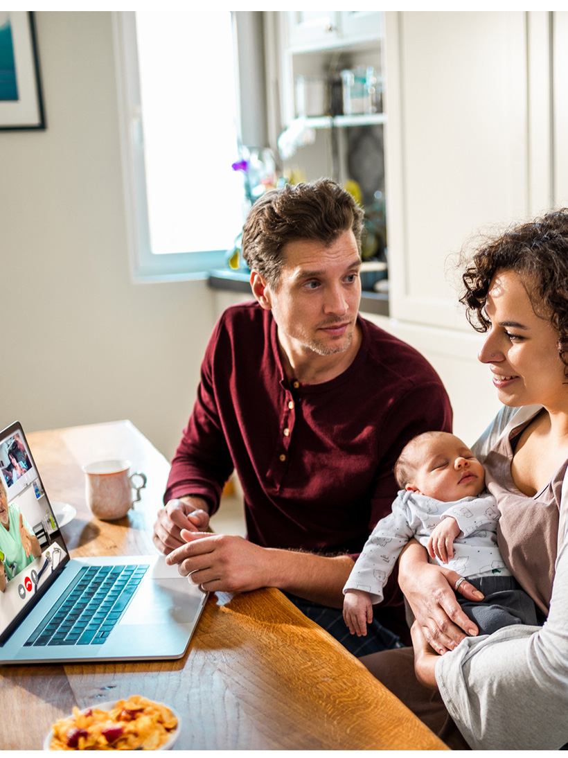 young father and mother holding baby while using laptop.